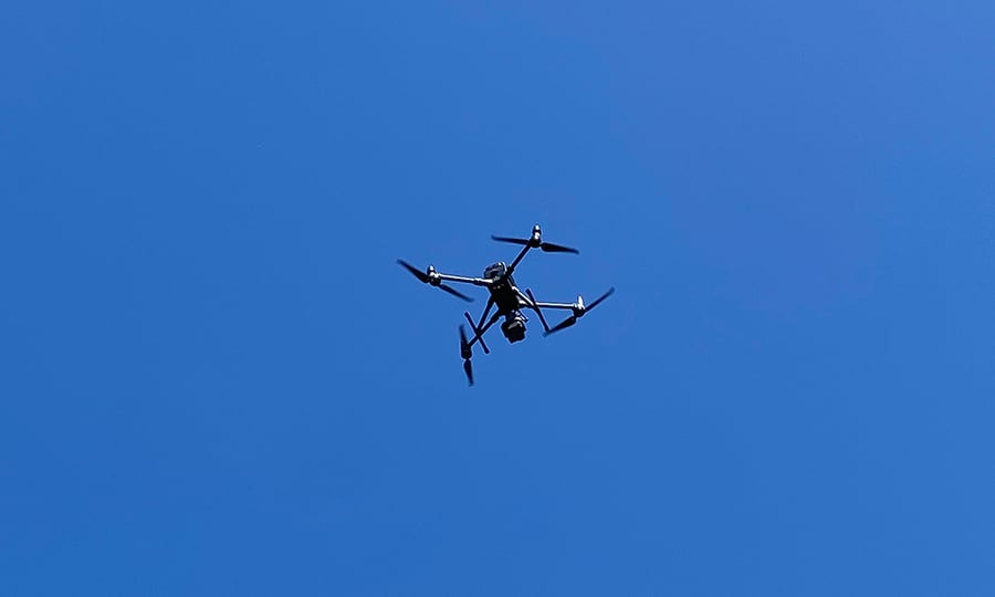 A drone flies in front of a clear blue sky.