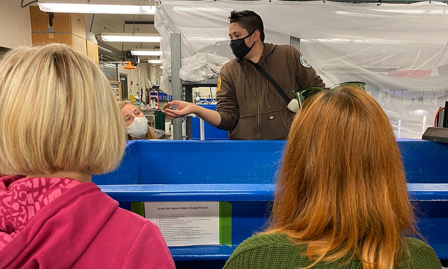An employee shows off an animal that grows in the tank that students are gathered around.