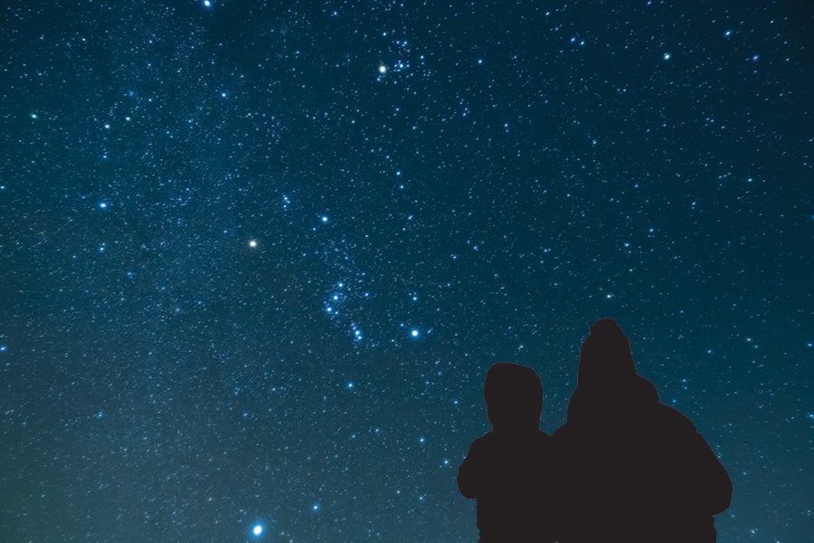 Two people in silhouette dressed in winter clothing look at the night sky.