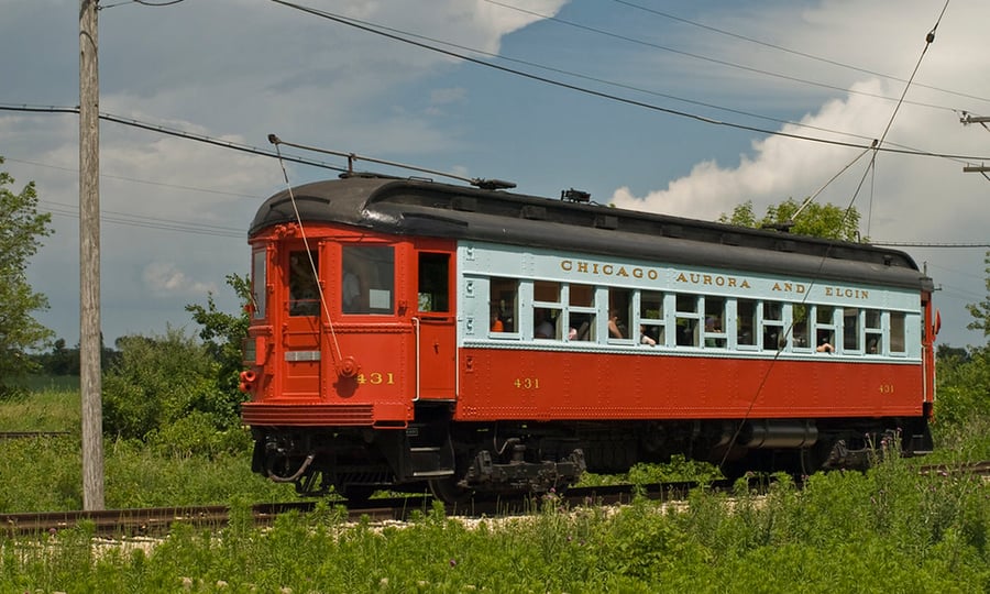 A green, white, and black train car connected to electrical lines.