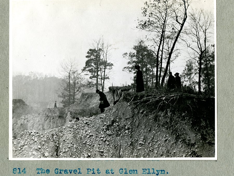 People stand on the edge of a gravel pit in this black and white photo.