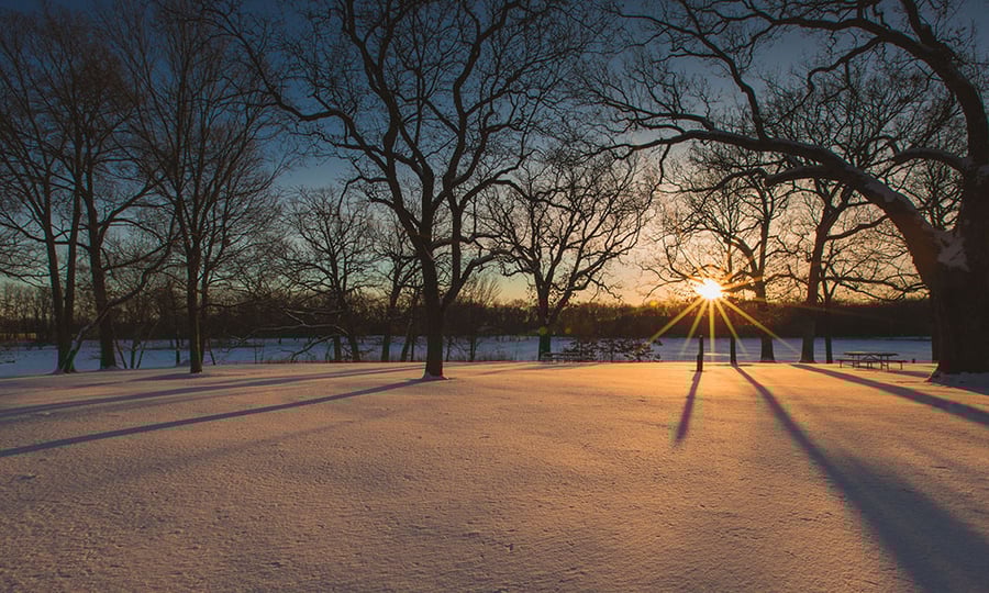 A sun sets over a lake and snow-covered field.
