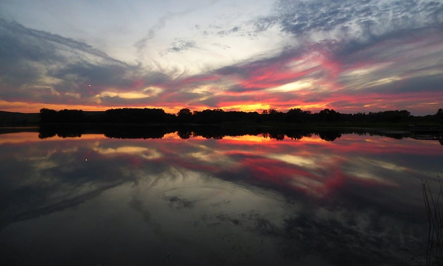 A purple, orange, and red sunset over a glassy lake that reflects the sky. 
