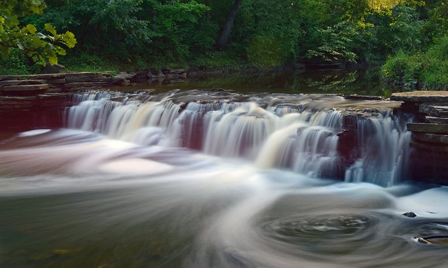 Water rushes over a manmade waterfall in a forest preserve.