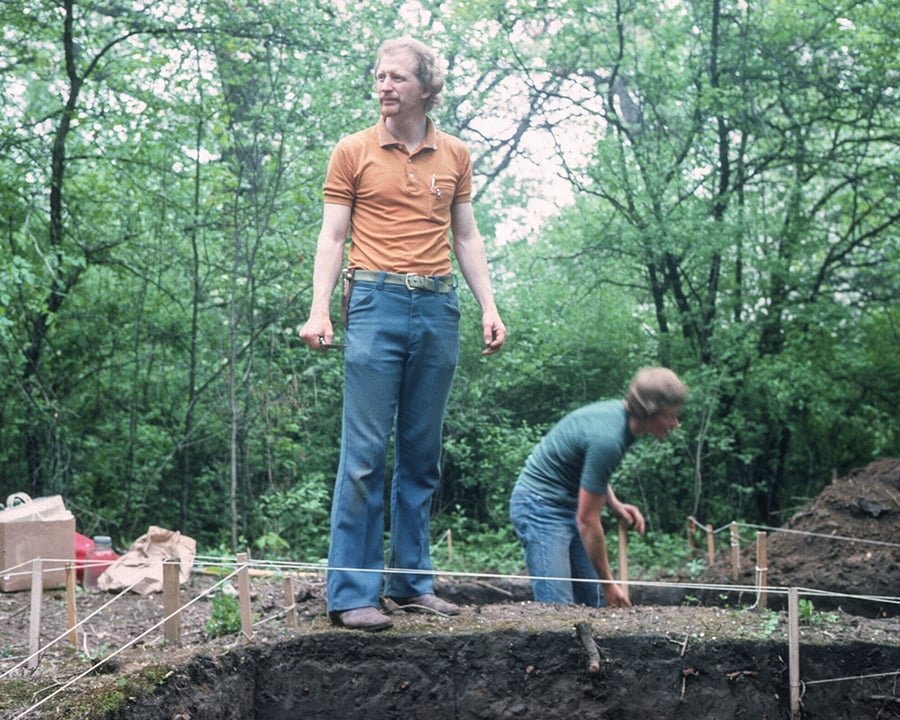A man stands above holes at a dig site.