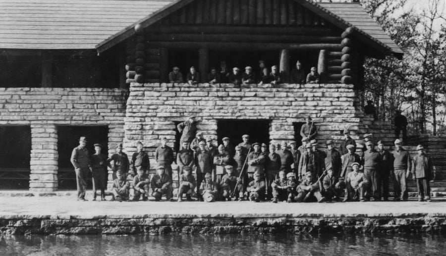 A group of young men stand around an old brick building.