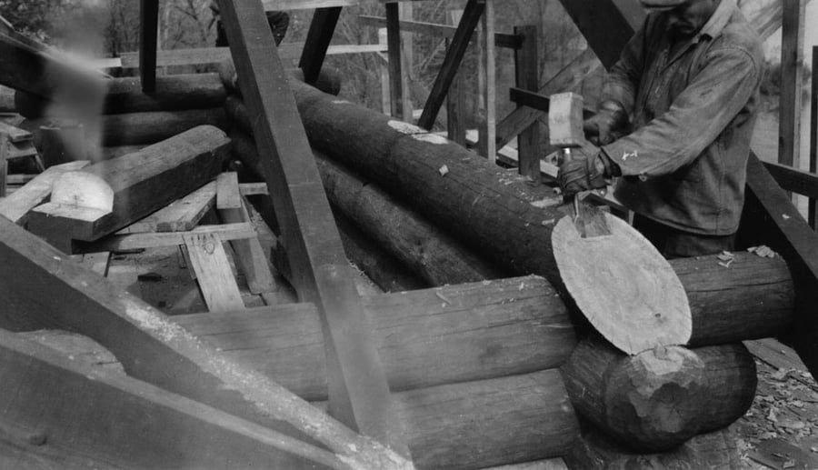 A man chisels a log into an angle.