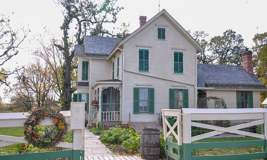 A 1880s farmhouse sits behind a white and green fence.