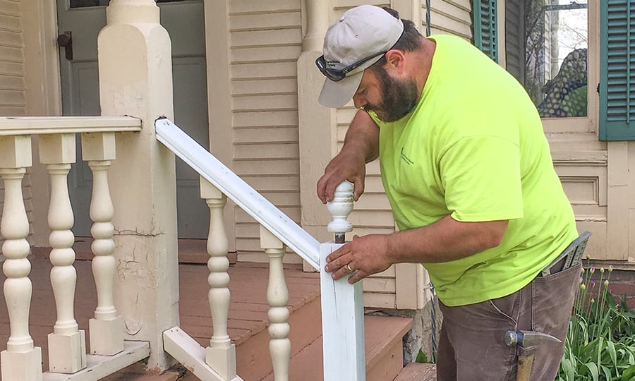 A carpenter in a high-vis shirt installs a newel post finial on a handrail.