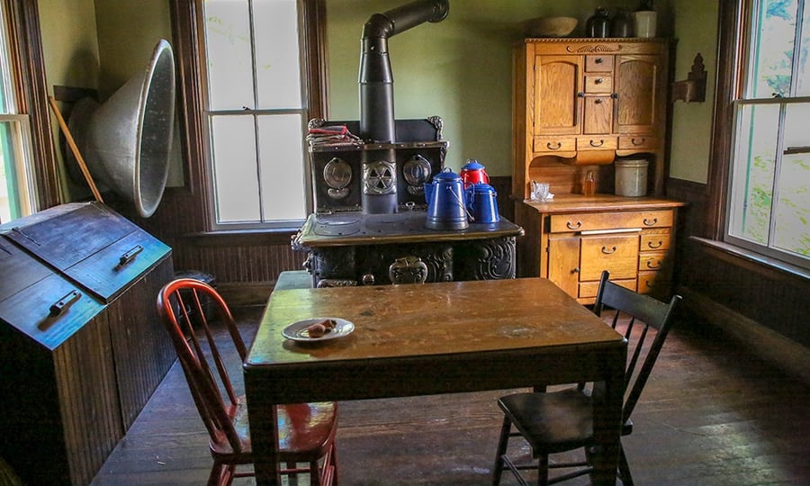 A kitchen table with two chairs sits in front of a wood-burning stove in the farmhouse's kitchen.
