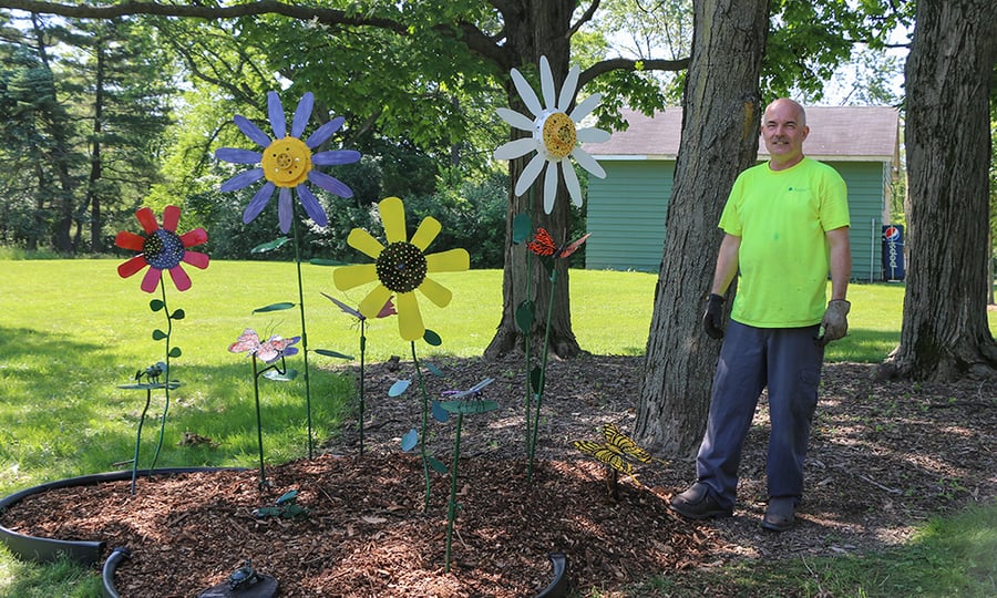 A man in a high-vis T-shirt stands near the metallic sculptures he created.