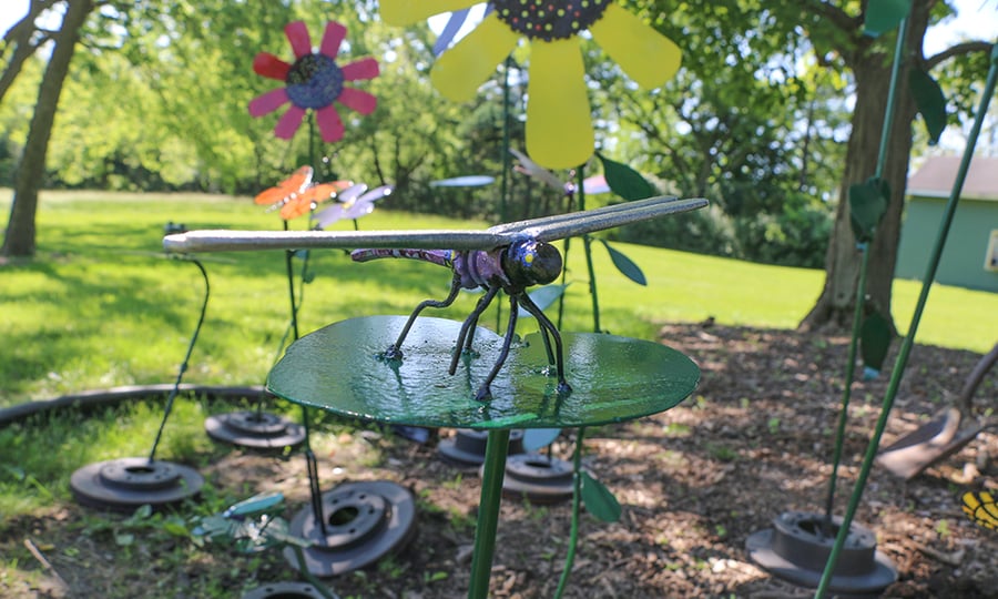 A metallic dragonfly sculpture stands among metallic flowers.