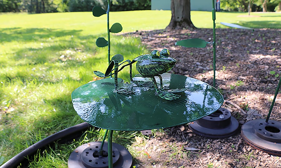 The finished frog sculpture is mostly green with bright yellow eyes.