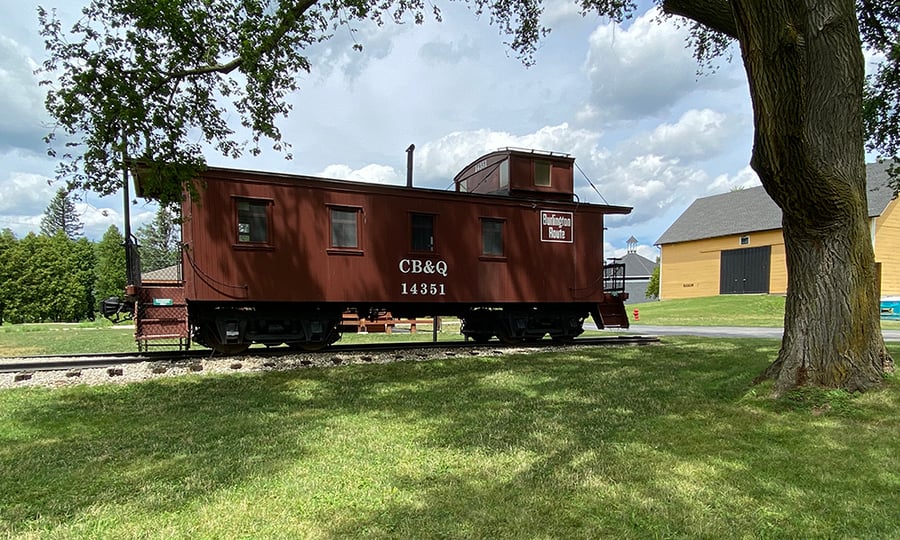 A caboose on a short set of tracks rests near the yellow barn.