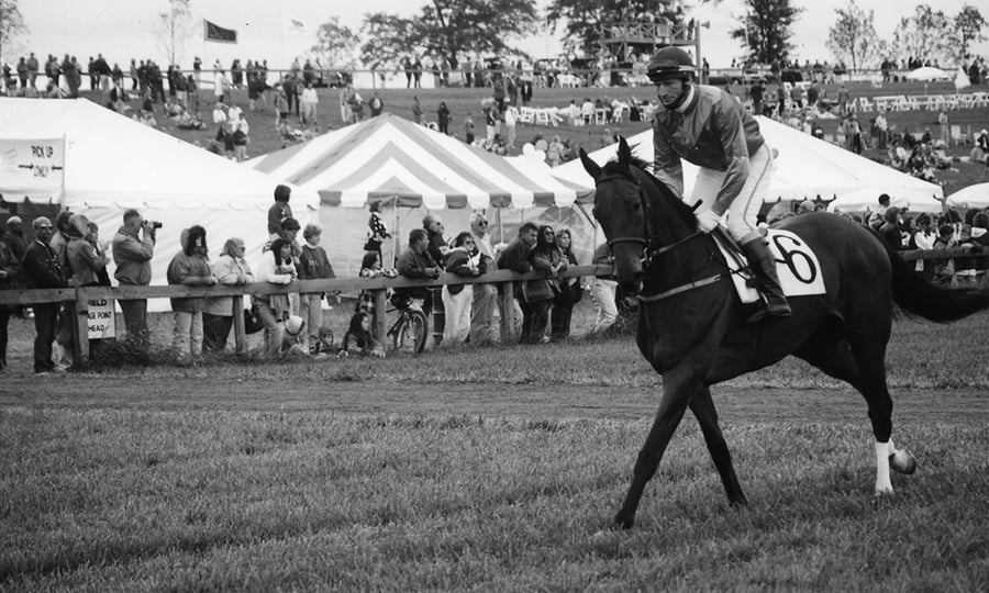 A jockey steers his course in front of a crowd in this old black and white photograph.