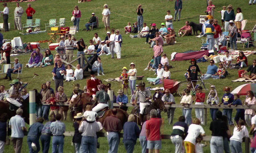 Crowd surrounds jockeys on horses.