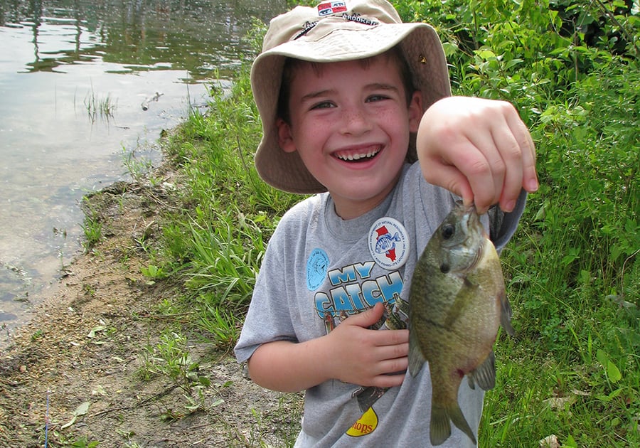 A boy in a buckethead raises a freshly caught fish.