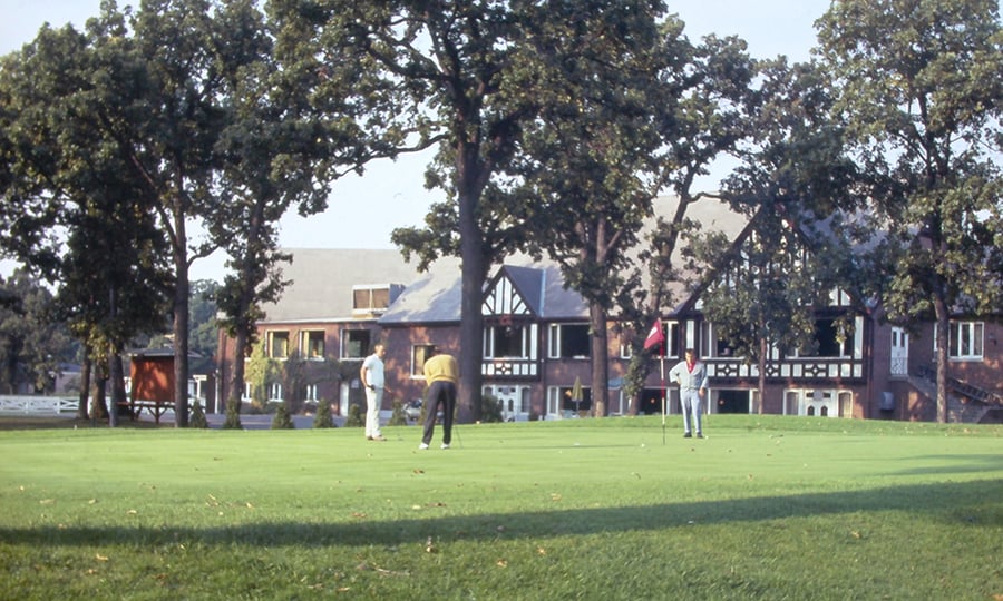 A man putts a golf ball while two others look on.