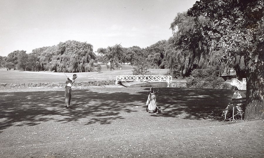 A golfer tees off in this black and white photograph.