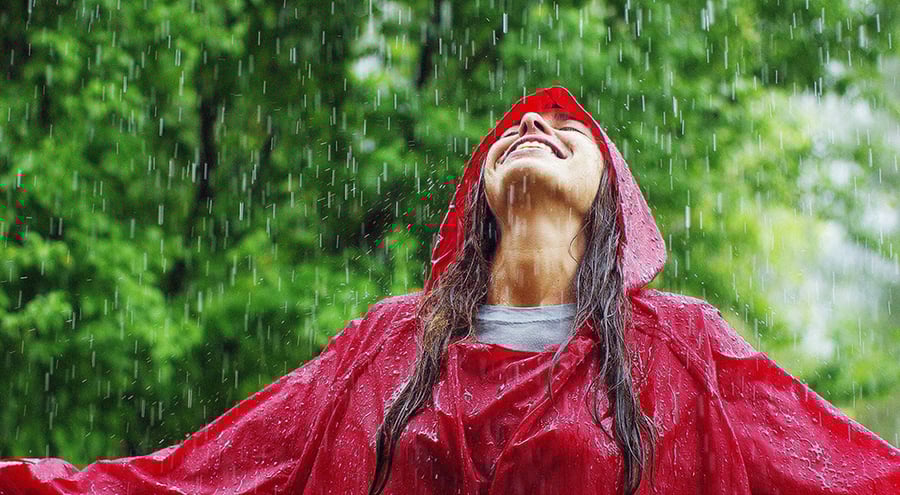 A woman in a poncho smiles up at a rainy sky.