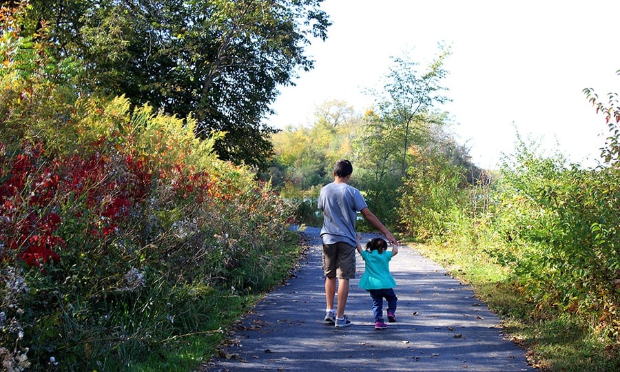 A boy guides a young girl down a trail in a forest preserve.