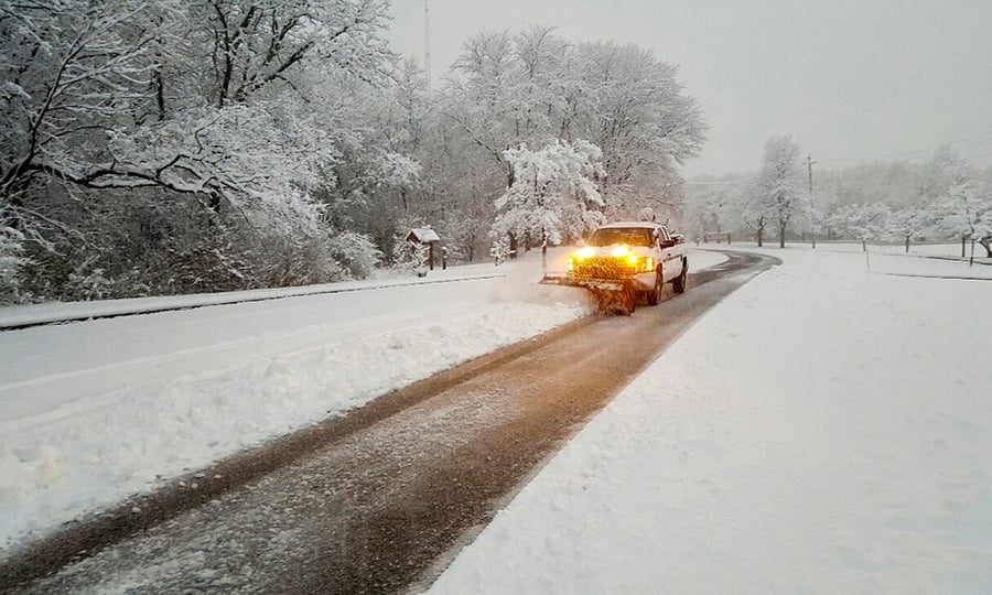 A white truck plows inches of snow from a road.