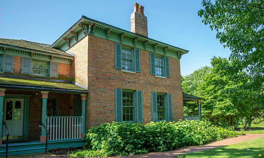 Green bushes surround an old brick home.