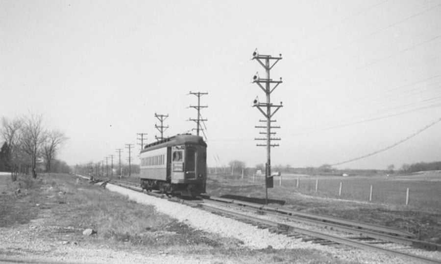A black and white photo shows a single train car passing electrical poles.
