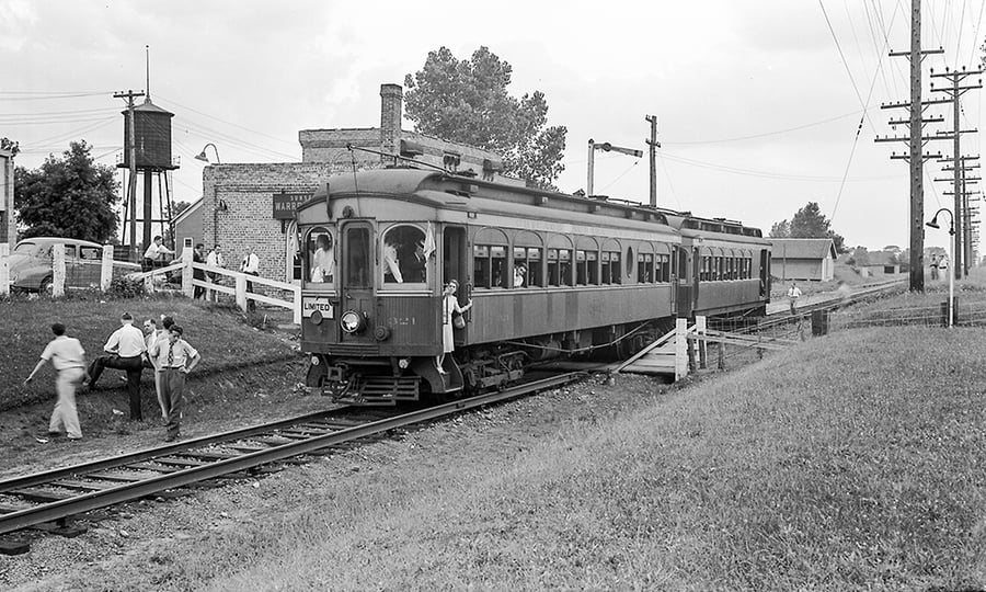 A black and white photo shows sharp-dressed people on and around the train.