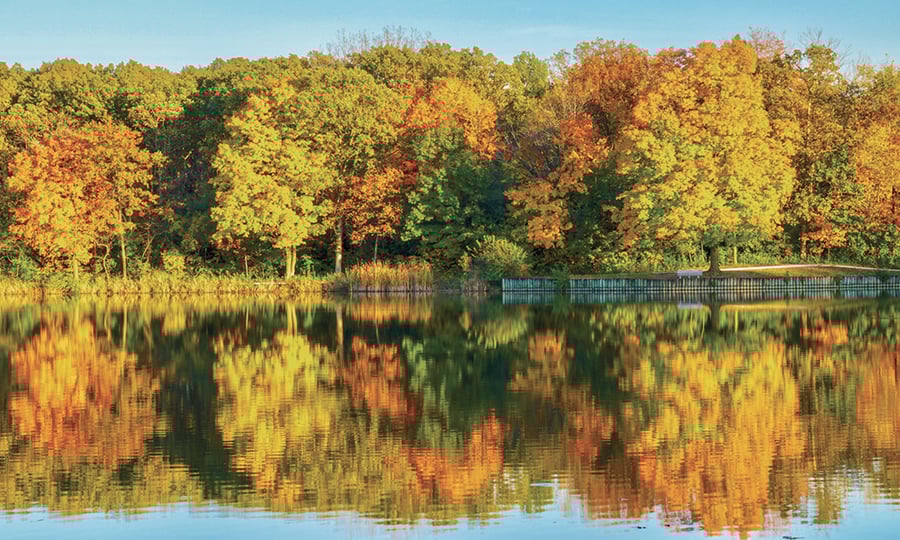 Images of colorful trees reflect off the surface of a calm lake.
