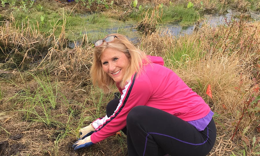 A volunteer in a pink jacket and gloves working with plants outside at the nursery.