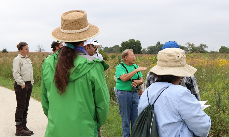 The group tour moves just off a trail near head high vegetation.