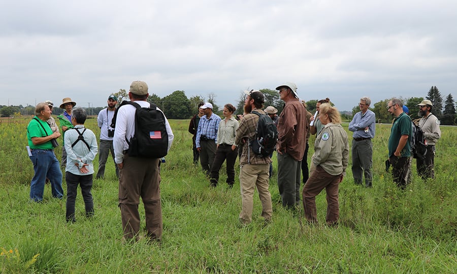 The group of ecologists and volunteers tour a grassy field.