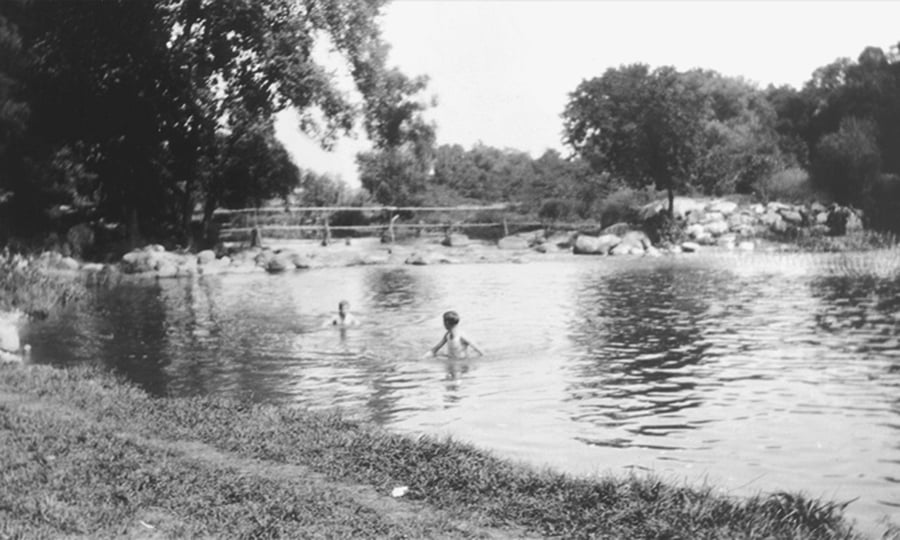Two boys wade in a river in an old photograph.