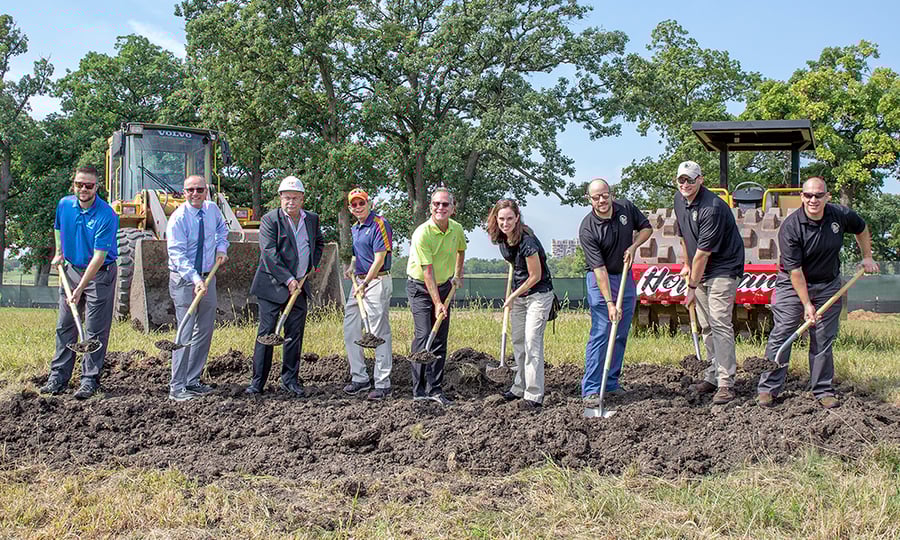 Eight men and one woman scoop dirt during a groundbreaking ceremony.