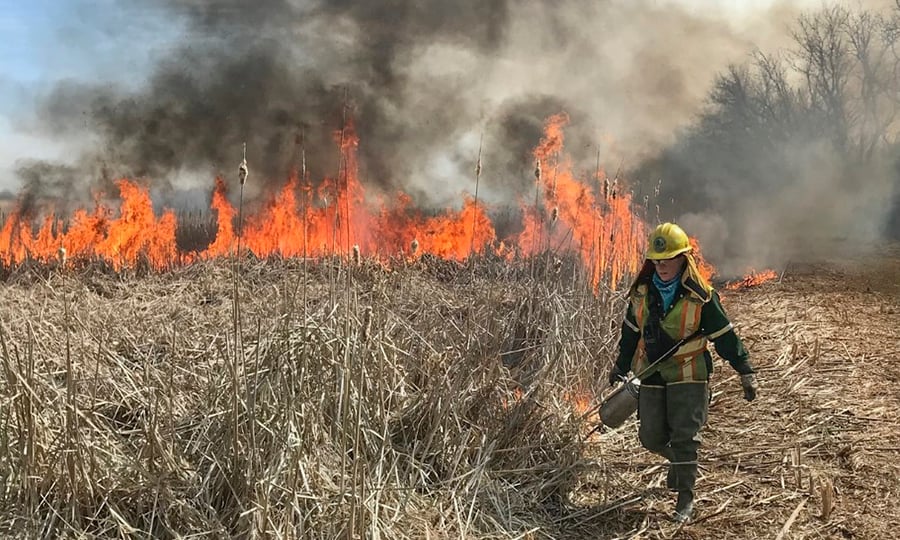 A woman walks away from a fire with a gas can.