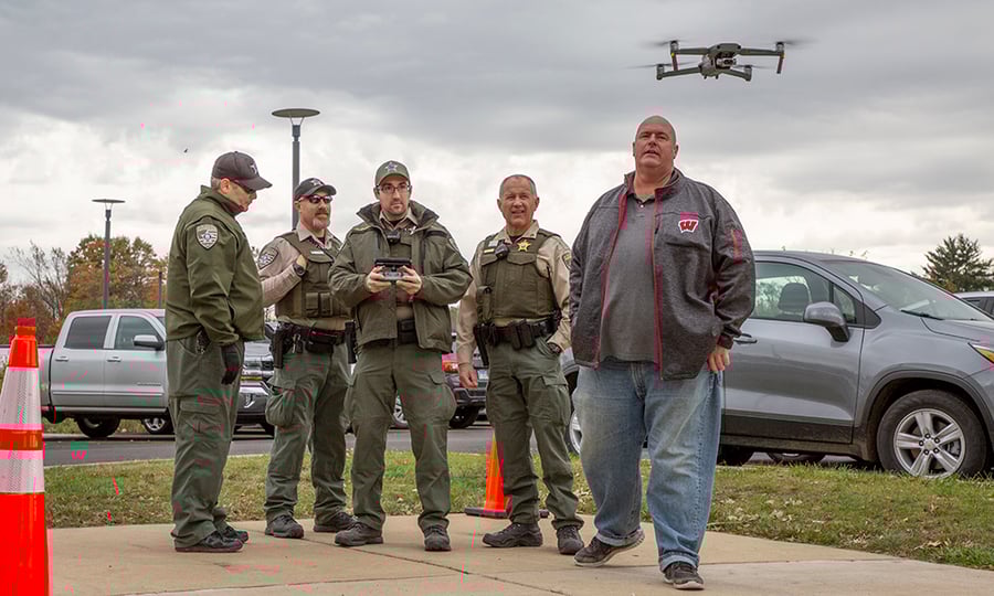 Four officers and an instructor watch a drone as it lands on a sidewalk.