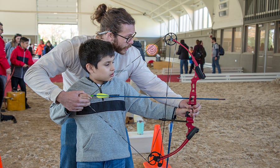 A District employee helps a boy shoot a bow and arrow.