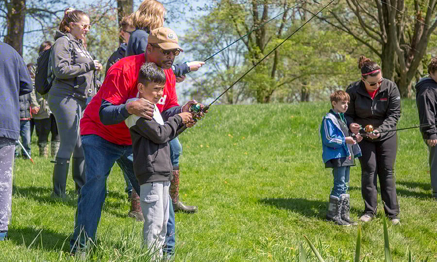 Children hold fishing poles as adults help them reel.