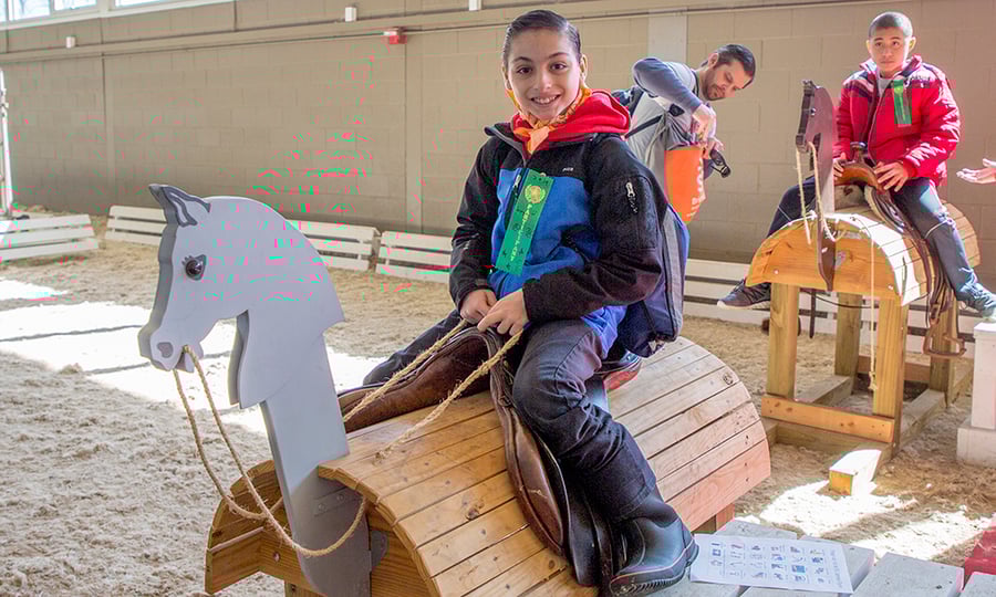 Boys sit in leather saddles on wooden horses.