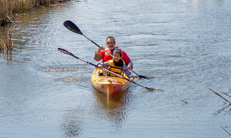 A man and a girl paddle a two-person kayak through calm water.
