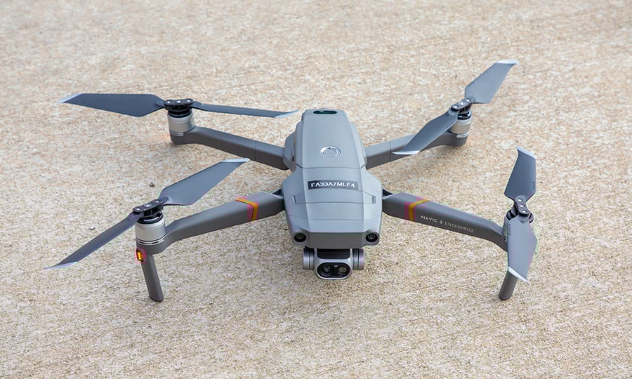 A drone with four blades and a camera sits on concrete.