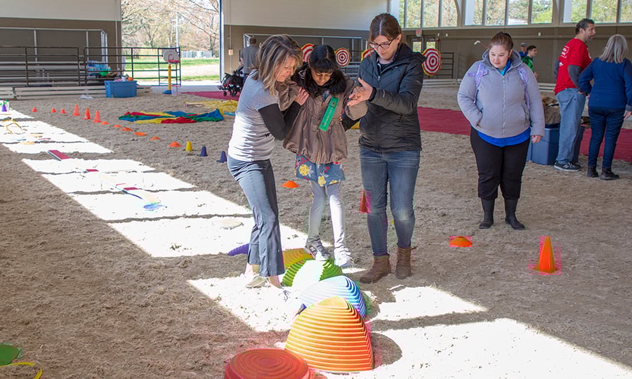 Two women help a girl navigate a colorful obstacle course.