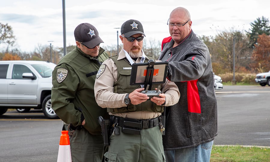 An instructor shows two officers how to operate a remote control for a drone.