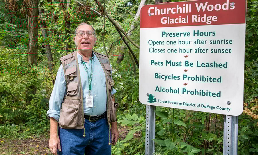 A man in a vest stands next to a Churchill Woods sign.