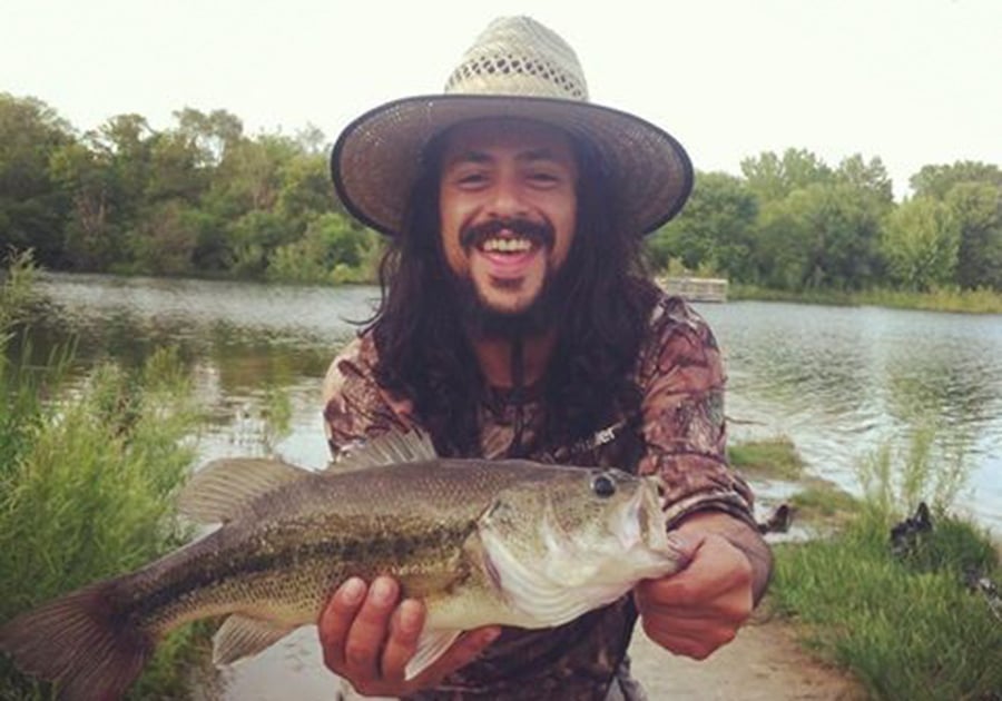 Standing on the shoreline in a straw hat and camo shirt, Jannotti holds up a nice-sized bass.