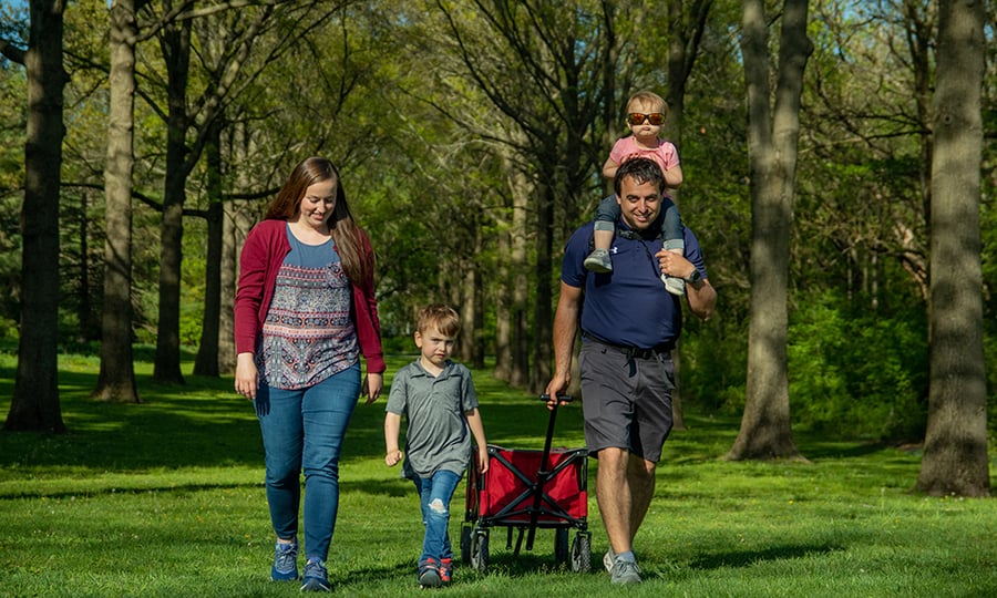 A family of four pulls a wagon through a tree-lined field.