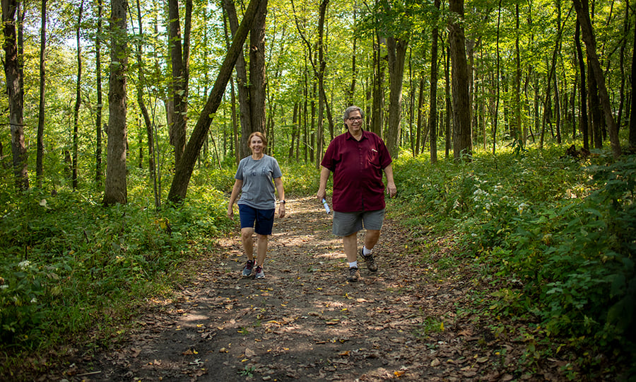 A woman and a man smile while hiking down a forest trail.