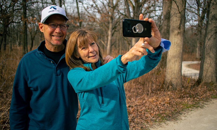 A couple stops to take a selfie on a hiking trail.