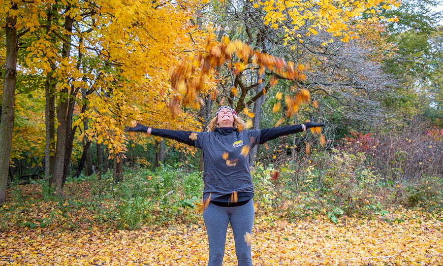 A woman smiles and throws fallen leaves in the air.